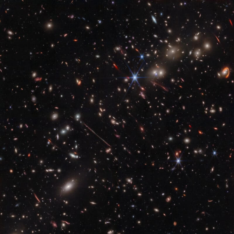 A dense field of stars and galaxies of various shapes and sizes scatters across the darkness of space. Some stars shine brightly with noticeable diffraction spikes, while many galaxies appear as spots or bright patches.