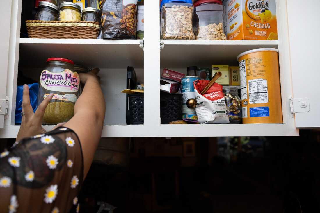 In this photo, Eloísa López reaches into a cabinet to grab a large glass jar with a handwritten label that says 