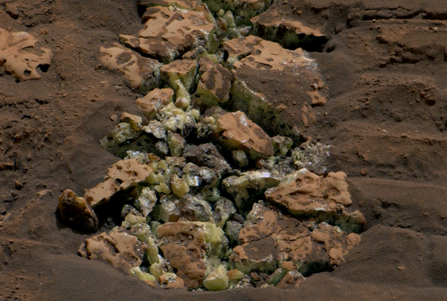 A photo of a Martian rock that has cracked to reveal yellow-green crystals.