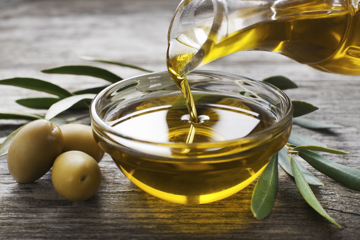 Bottle pouring virgin olive oil into bowl close up