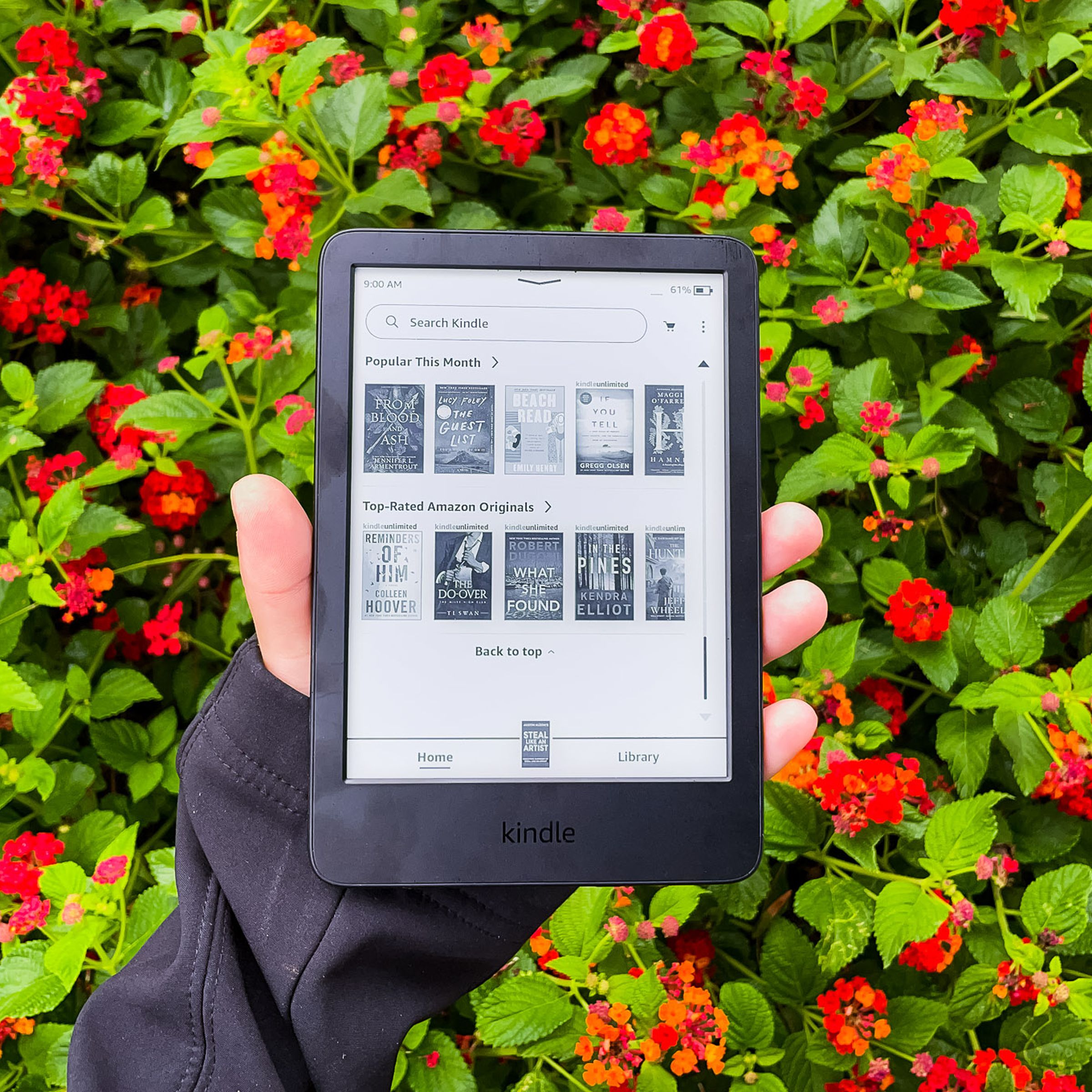 A hand holding Kindle 2022 in front of red flowers.