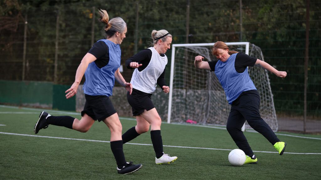 Three women playing football on a field