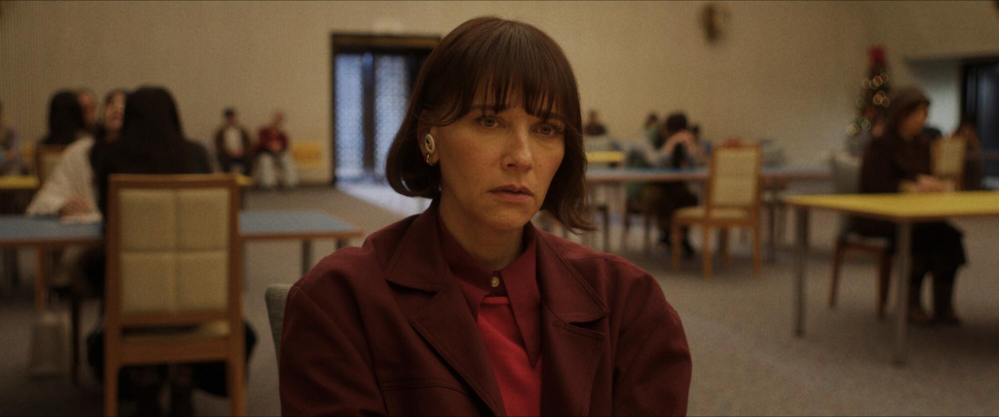 A woman with short hair wearing a brown jacket and shirt sitting at a table.