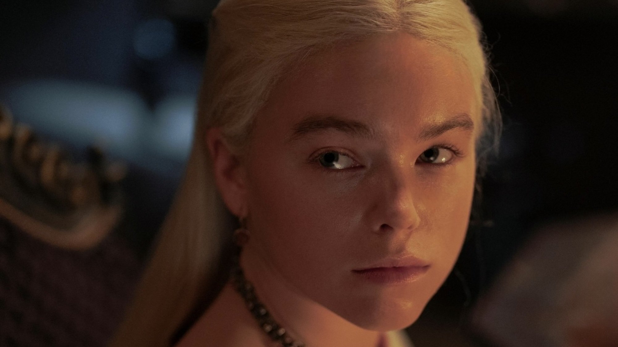 Close-up of young Rhaenyra Targaryen's face, lit by the fire in a nearby fireplace.