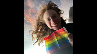 Haley Arceneaux holding a pride flag in front of a window, with the Earth behind