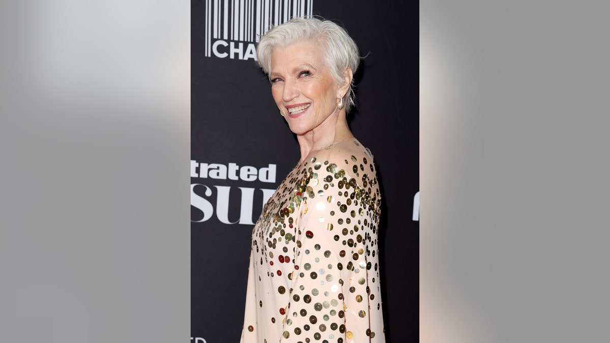 Maye Musk looks to the side and smiles in a shimmering gold and beige dress.