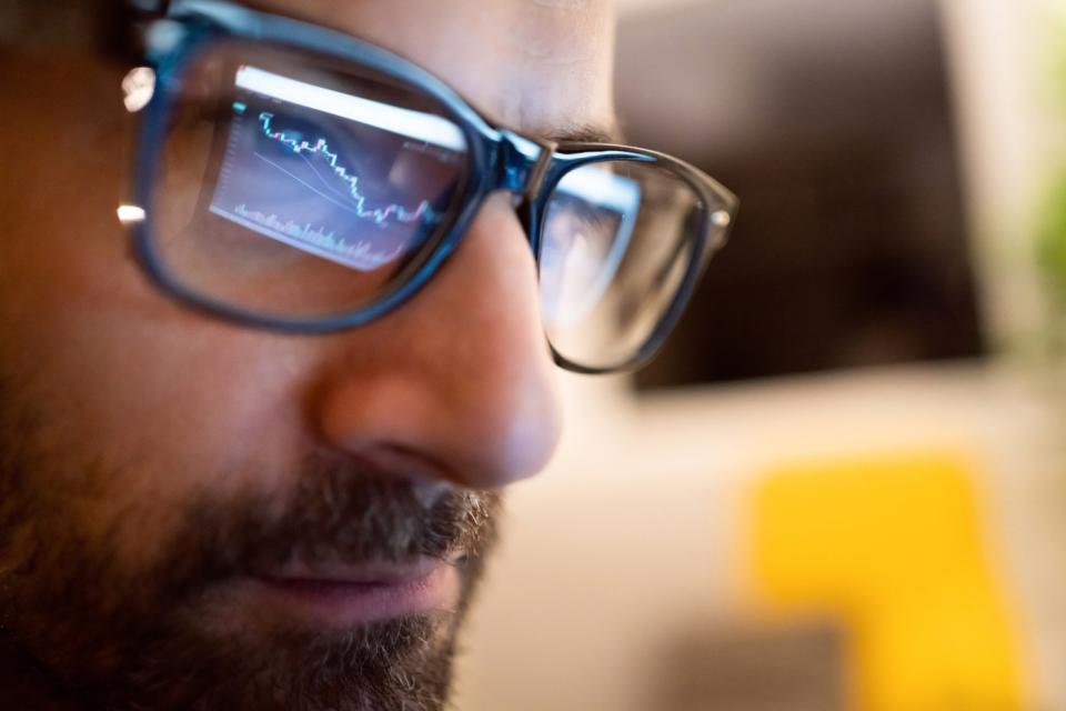 A stock chart reflected in the glasses of a professional investor looking at a computer screen.