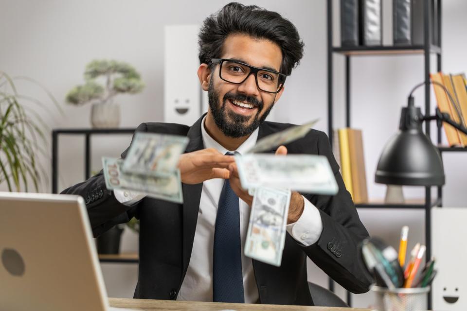 A happy person in a suit throwing dollar bills on a desk. 