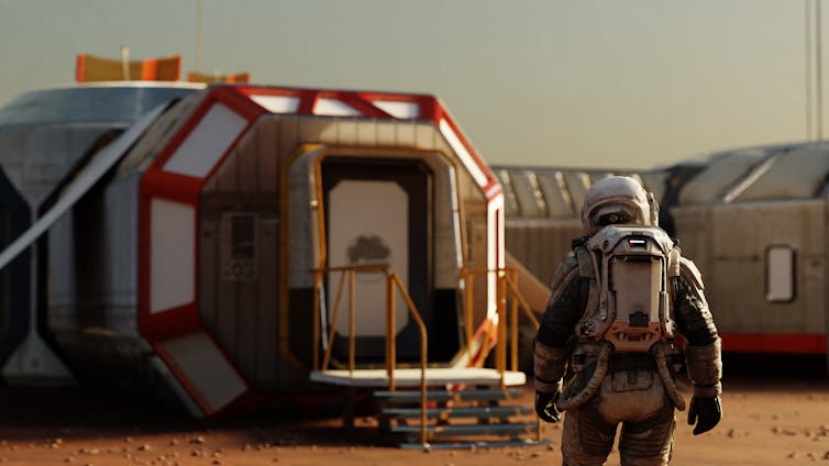 An illustration shows an astronaut on Mars, standing in front of a red, white and silver modular habitat.