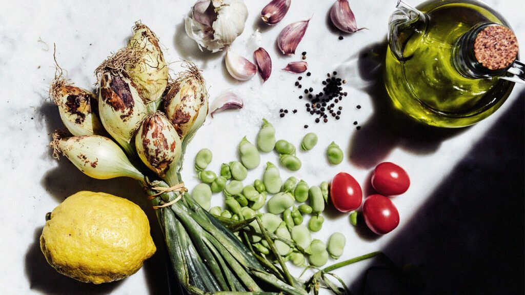 photo of spring onions, lemons, garlic cloves, cherry tomatoes, beans and olive oil