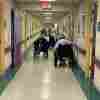 Three people in wheelchairs move down the hallway of a retirement home. 