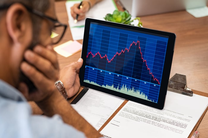 A visibly worried person looking at a rapidly rising and then falling stock chart displayed on a tablet.