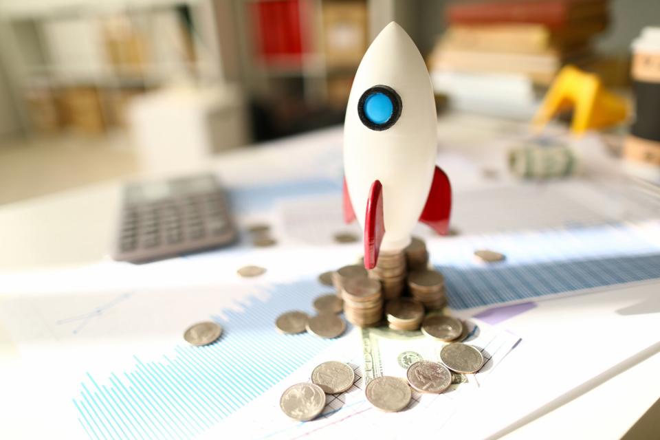 A toy rocket ready to launch atop a pile of coins and documents displaying financial information. 