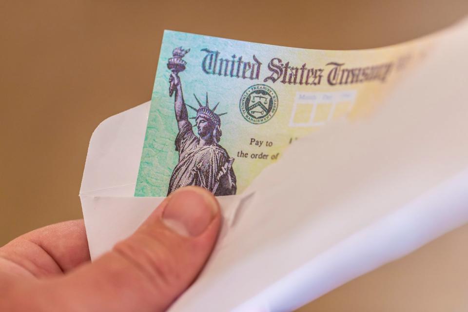 Hand holding an envelope containing a check from the US Treasury.