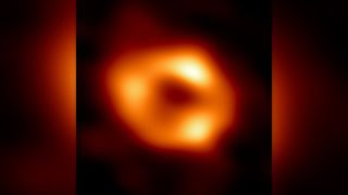 Telescope image of a black hole, revealed as a fuzzy donut of yellow-orange light surrounding a black center