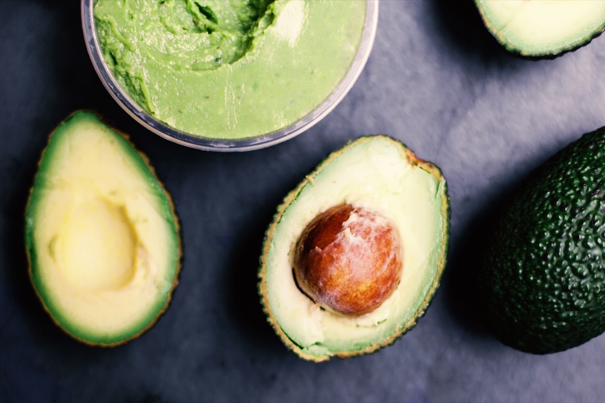 avocado cut in two halves near a bowl of guacamole on a black surface