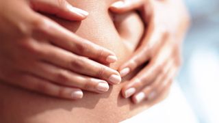 Close-up of a person holding his hands on his stomach. Only a small part of the stomach is visible, where the navel is. The background is blurred.