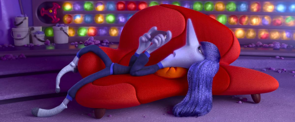 Ennui lies on her back on a bright red couch, looking irritated and playing with her phone, in a scene from Pixar Animation Studios' Inside Out 2.