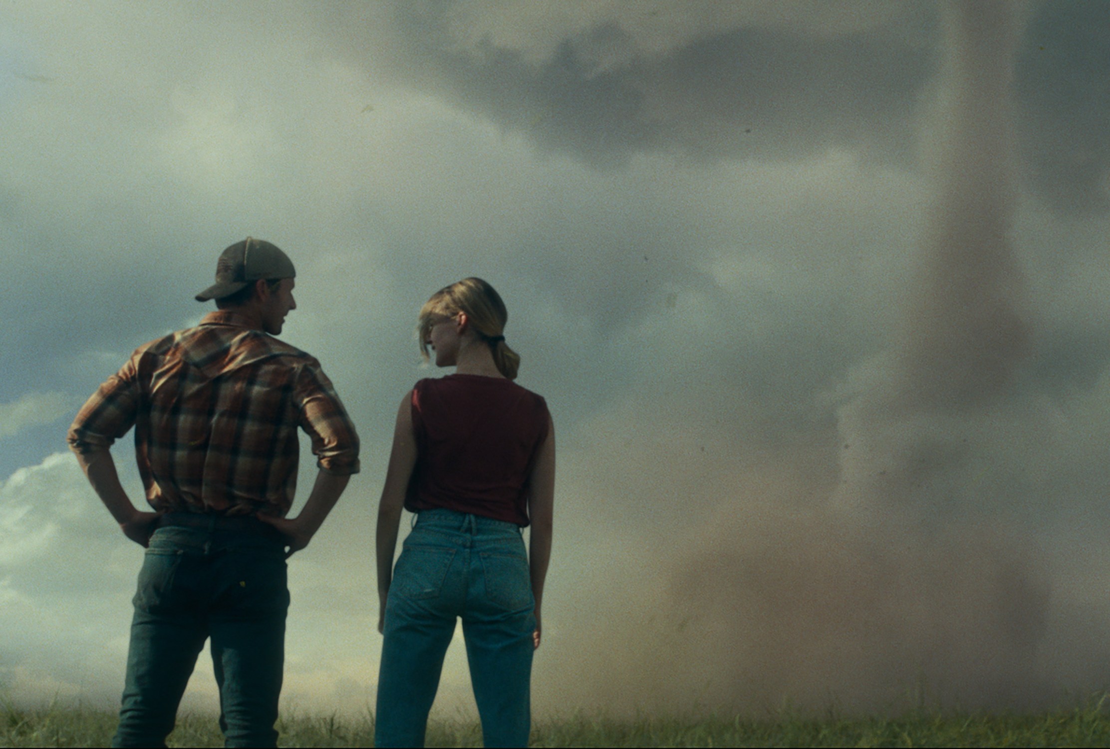 A man and a woman stand with their backs to the camera, facing a swirling cloud.