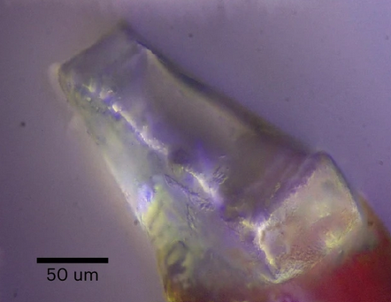 Microscopic photograph of a purple and green crystal. A scale indicates that the image is about 200 micrometers in diameter.