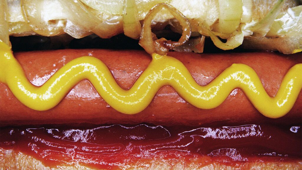 Close-up of a hot dog with mustard, ketchup and onions, representing ultra-processed foods