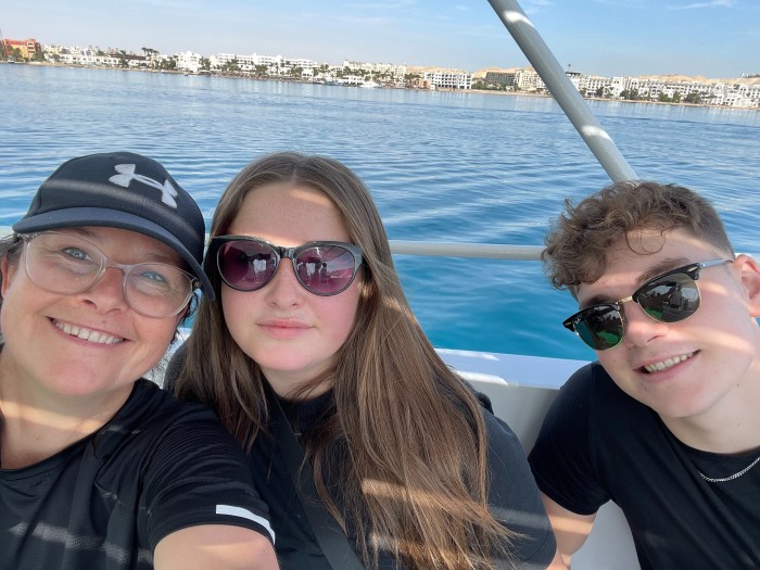 A middle-aged woman and a teenage boy and a girl pose for a selfie on a boat